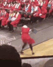 a woman in a red dress is dancing on a stage in front of a crowd of people wearing red caps and gowns .