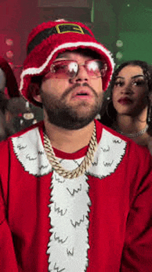 a man wearing a santa hat and sunglasses is standing next to a woman wearing a santa suit .