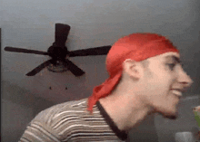 a man wearing a red headband and a striped shirt is smiling in front of a ceiling fan