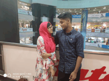 a man and a woman are posing for a picture with a redmi note 7 pro in the foreground