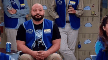 a man with a beard is sitting in front of a group of lockers with a can of soda .