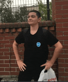 a young man in a black shirt is standing in front of a brick wall holding a bag that says evre