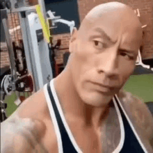 a bald man in a tank top is standing in a gym .