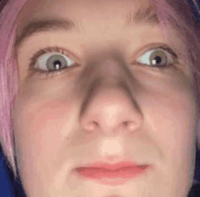 a close up of a person 's face with pink hair making a funny face .