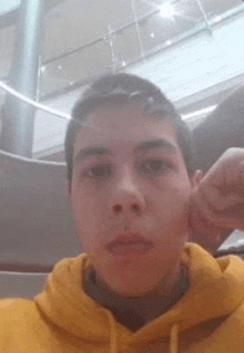 a young man in a yellow hoodie is taking a selfie in a mall .