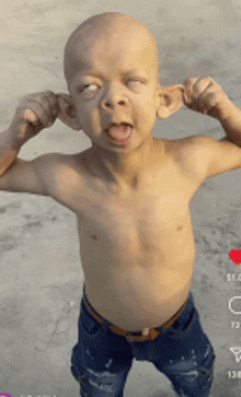 a shirtless child is making a funny face with his hands in his ears