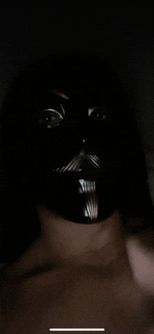 a person wearing a black mask with a mustache on their face in the dark .