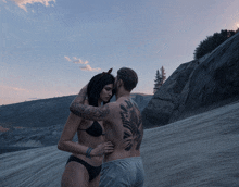 a man with a tattoo on his back is hugging a woman in a black bikini