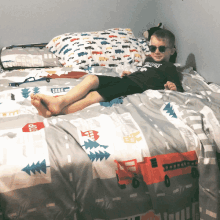 a young boy wearing sunglasses is laying on a bed with a blanket that says texas