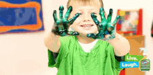 a young boy with his hands covered in green paint stands in front of a sign that says " live laugh "