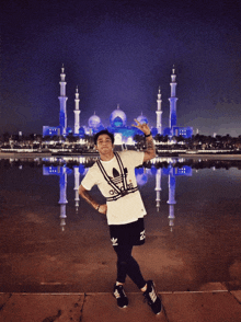 a man in a white adidas shirt stands in front of a mosque