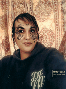 a woman with a dragon tattoo on her face wears a black hoodie