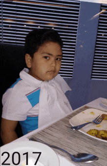 a young boy sits at a table with a plate of food in front of him and the year 2017