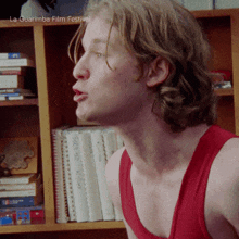 a man in a red tank top is standing in front of a bookshelf with la guarimba film festival written on the bottom right