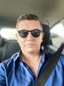 a man wearing sunglasses and a blue shirt sits in a car