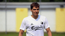 a man wearing a white adidas carlsberg shirt stands on a field