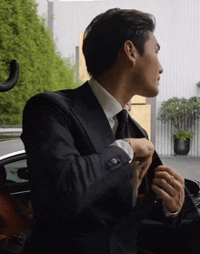 a man in a suit adjusts his jacket while getting out of a car