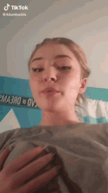 a girl is wearing a grey shirt and making a funny face while holding her chest .