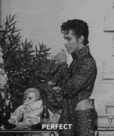 a black and white photo of a man standing in front of a table with a bottle of wine and a statue .