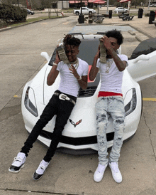 two young men sitting on the hood of a white sports car holding stacks of money