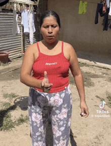 a woman wearing a red tank top and floral pants is standing in front of a clothes line