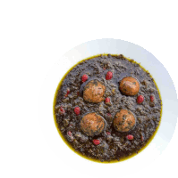 a bowl of stew with eggs and pomegranate seeds on a white plate