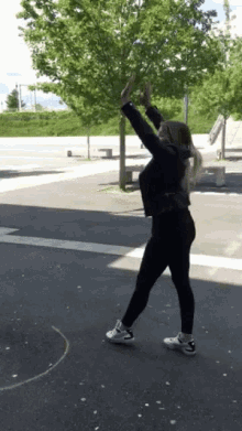 a woman in a black jacket and black pants is standing on a street with her arms in the air