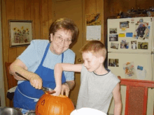 an elderly woman helps a young boy carve a pumpkin in front of a refrigerator