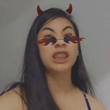 a woman wearing devil horns and flaming sunglasses makes a funny face