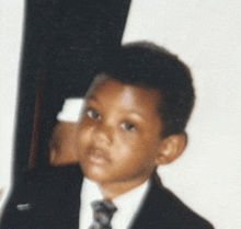 a young boy wearing a suit and tie is looking at the camera