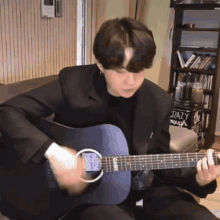 a man in a black suit is playing an acoustic guitar in front of a bookshelf that says crazy enough