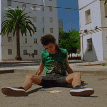 a man is sitting on the ground in front of a building with la guarimba film festival written on the bottom right