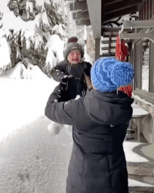 a woman in a black jacket is holding a child in her arms in the snow .