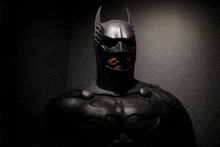 a man in a black batman costume stands in the dark