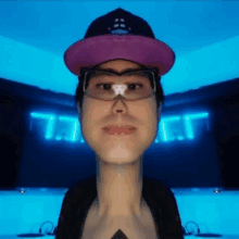 a man wearing a purple hat and glasses is standing in front of a blue background with the letter t on it