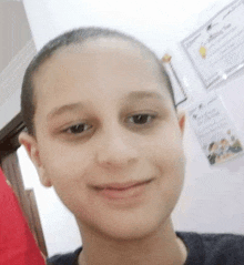 a young boy with a shaved head is smiling and taking a selfie .