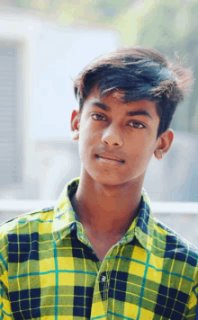 a young boy wearing a yellow and black plaid shirt looks at the camera