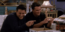 two men are laughing and pointing at a cardboard box that says 2 in 1 giant bottles