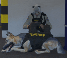 a sheriff sitting next to a dog with a vest that says sheriff on it