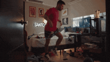 a man is dancing in a bedroom with a sign that says santo on the wall