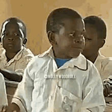 a group of children are sitting in a classroom . one of the children is making a funny face .