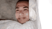 a man is laying in bed with a blanket on his head and smiling .