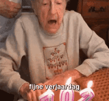 an elderly woman is blowing out candles on a birthday cake with the words fijne verjaardag written on the bottom