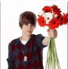 a boy in a plaid sweater is holding a bouquet of red and white flowers