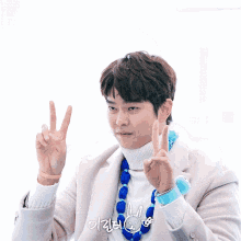 a man wearing a turtleneck sweater and a blue necklace giving the peace sign