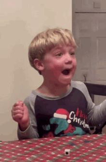 a young boy wearing a merry christmas shirt looks surprised