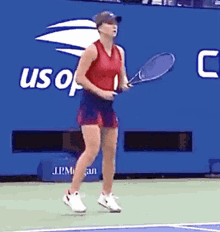 a woman is holding a tennis racquet on a tennis court in front of a blue wall that says us open