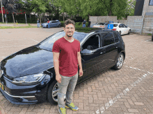 a man in a red shirt is standing in front of a car