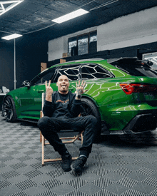 a man sitting in a chair in front of a green car