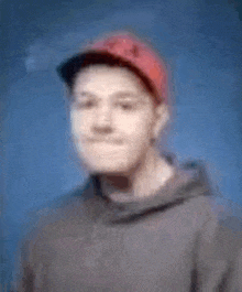 a blurry picture of a man wearing a red hat and a grey hoodie .